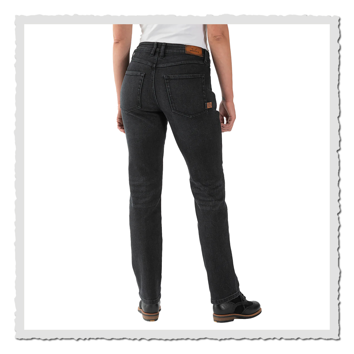 Person in schwarzer Jeans von hinten vor hellem Hintergrund, mit weißem Oberteil und schwarzen Schuhen.